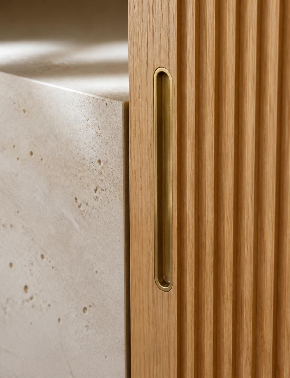 Oak joinery meeting travertine with a recessed brass pull